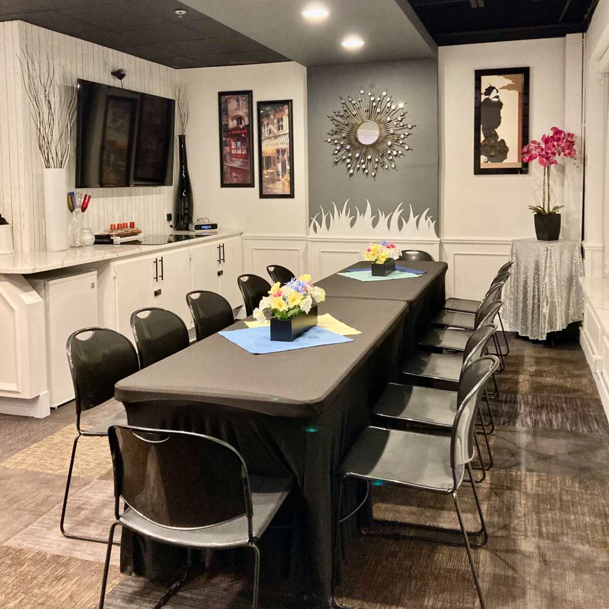 A meeting room features a long dark table surrounded by black chairs, with a television, framed artwork, and decorative elements on the walls.