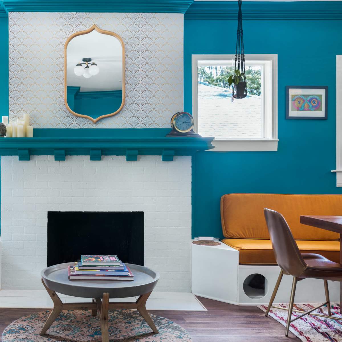 The room features a bright blue wall with a mirrored mantel above a white brick fireplace, flanked by large windows and decorated with comfortable seating and a round coffee table.