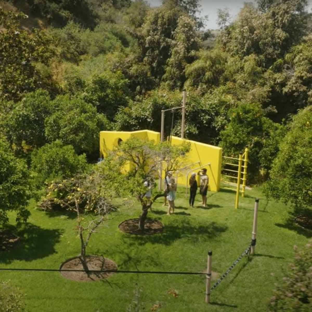 A vibrant backyard with a yellow play structure surrounded by trees and well-maintained grass.