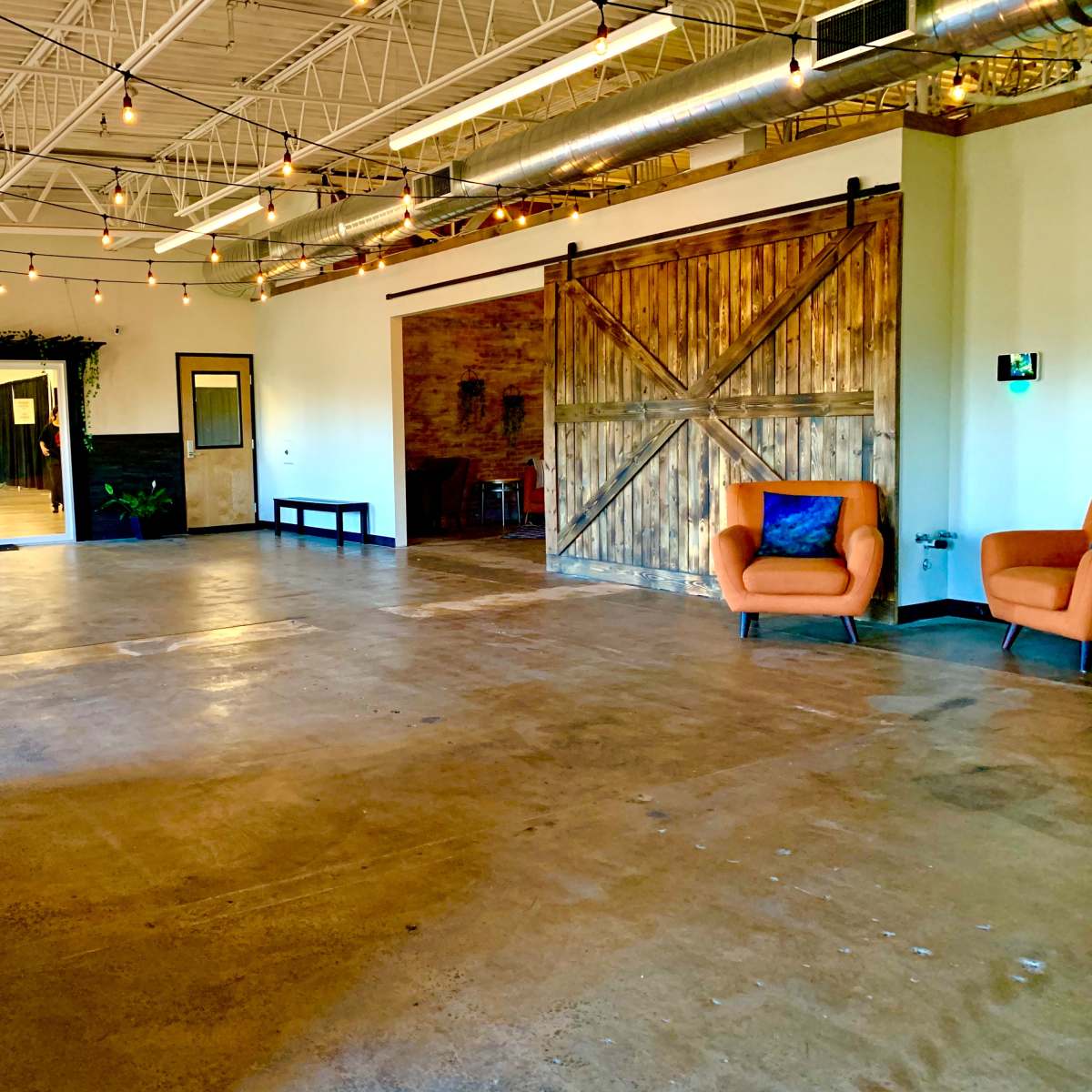 An empty indoor space featuring a polished concrete floor, a large sliding barn door, and a cozy orange armchair.
