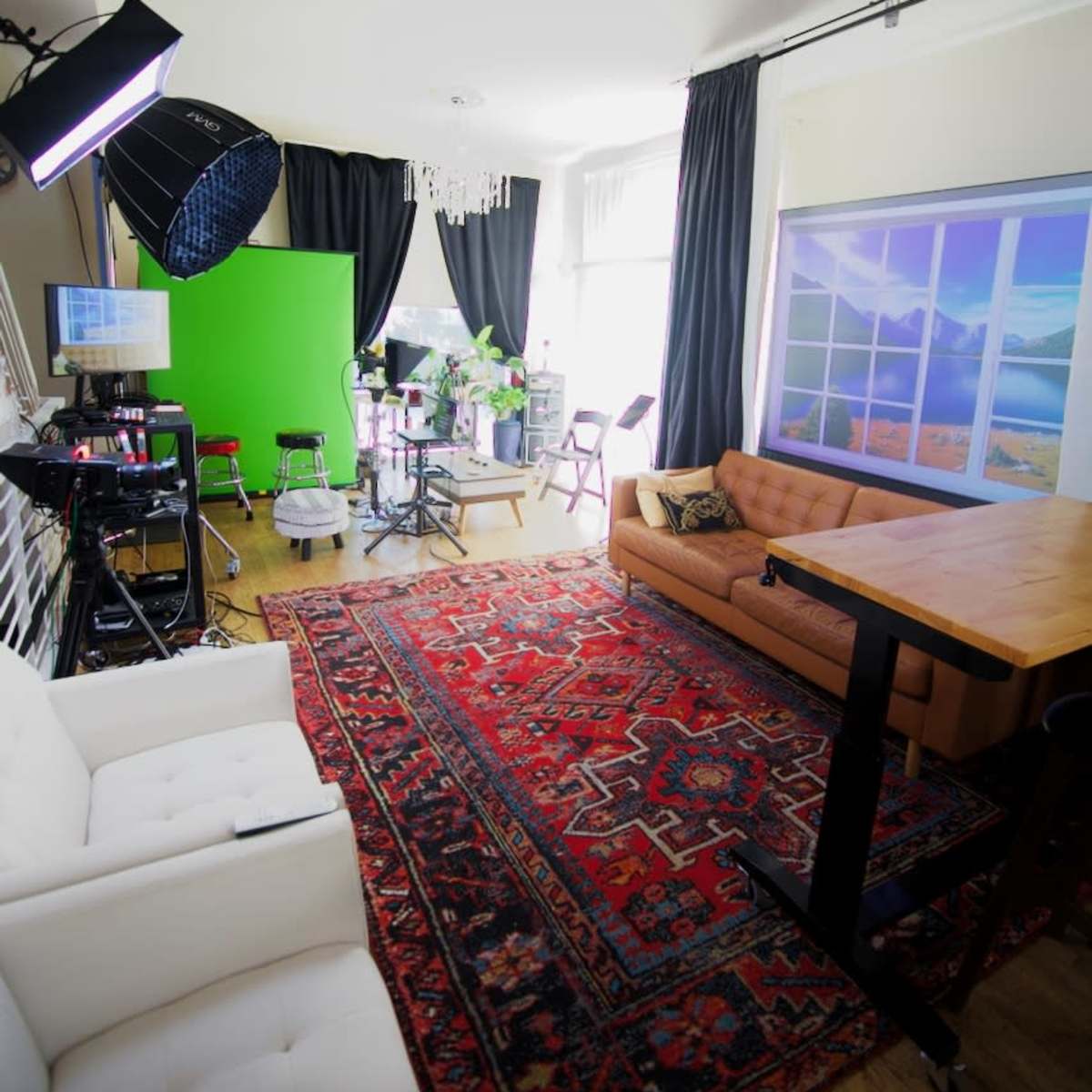 A bright studio space featuring a green screen, a beige couch, a wooden table, and a decorative rug.