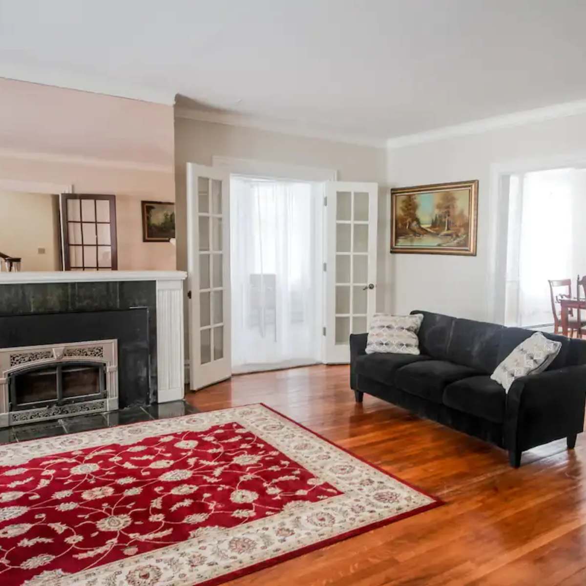 A living room features a black couch on a red rug, with a fireplace and French doors leading to other spaces.