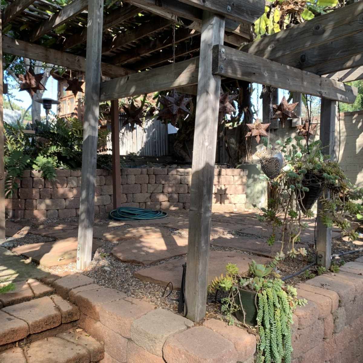 A landscaped garden area with stone pathways, wooden structures, and potted plants.