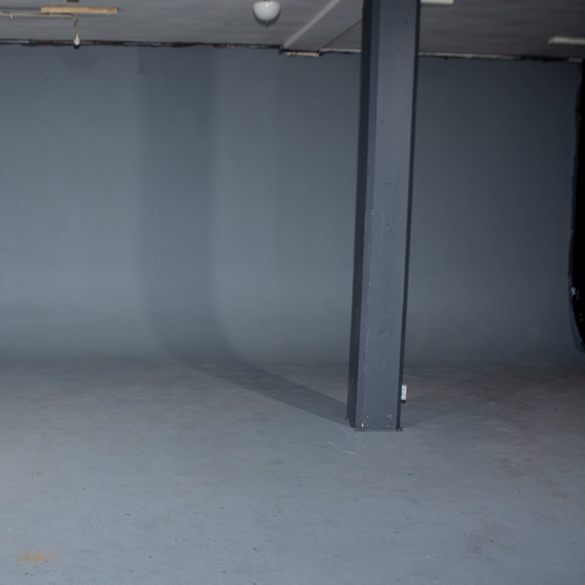 An empty studio space features a gray backdrop and a concrete floor with a centrally located dark column.
