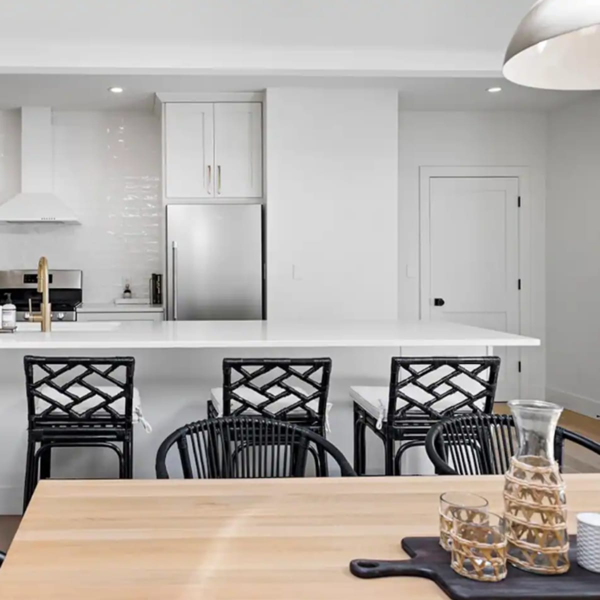 A modern kitchen features a white countertop island with four black bar stools, complemented by stainless steel appliances and minimal decor.
