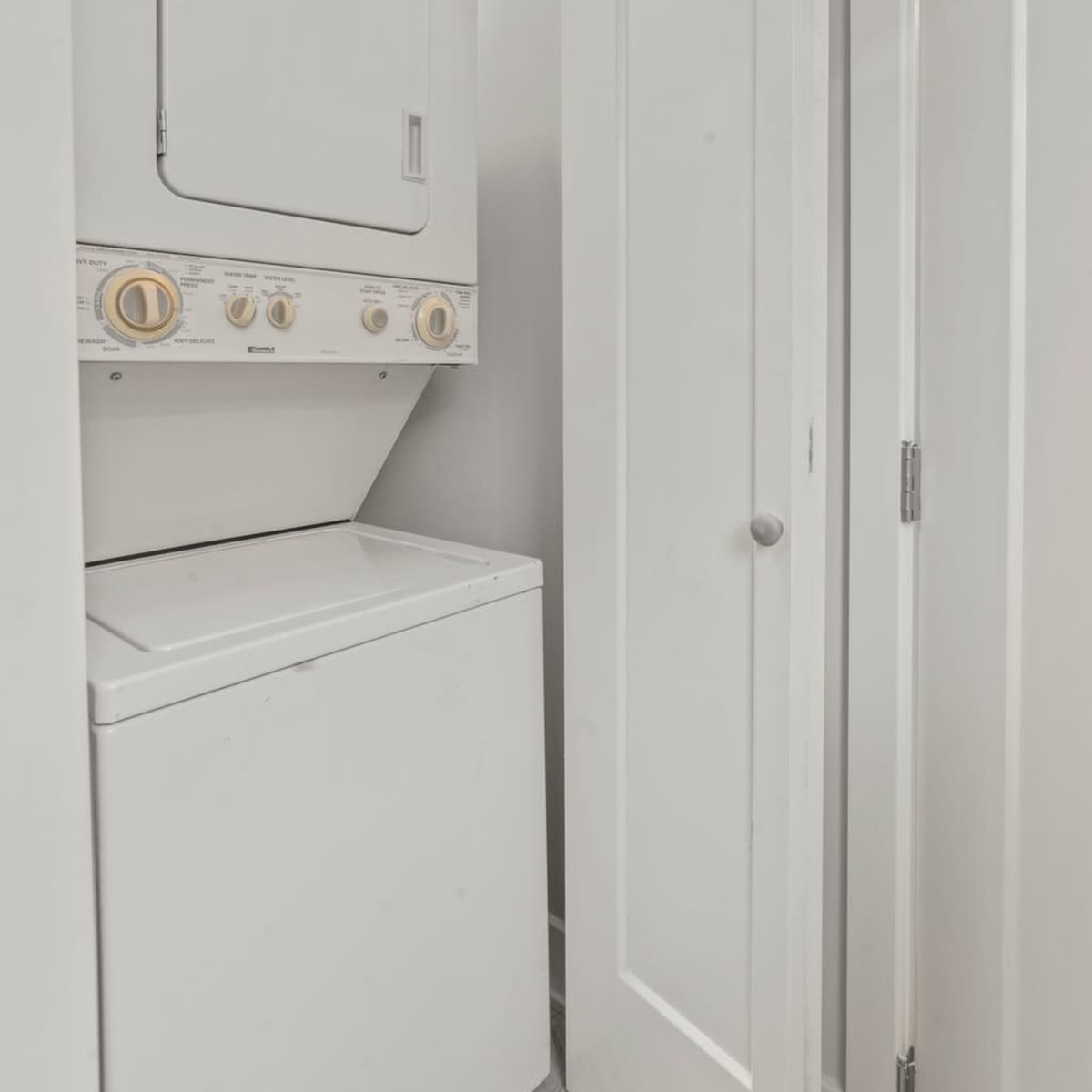 A compact laundry area with a stacked washer and dryer next to a closed white door.