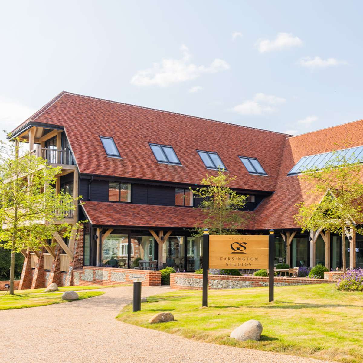 A modern hotel building with a stone and timber structure, surrounded by greenery and a gravel path leading to the entrance.