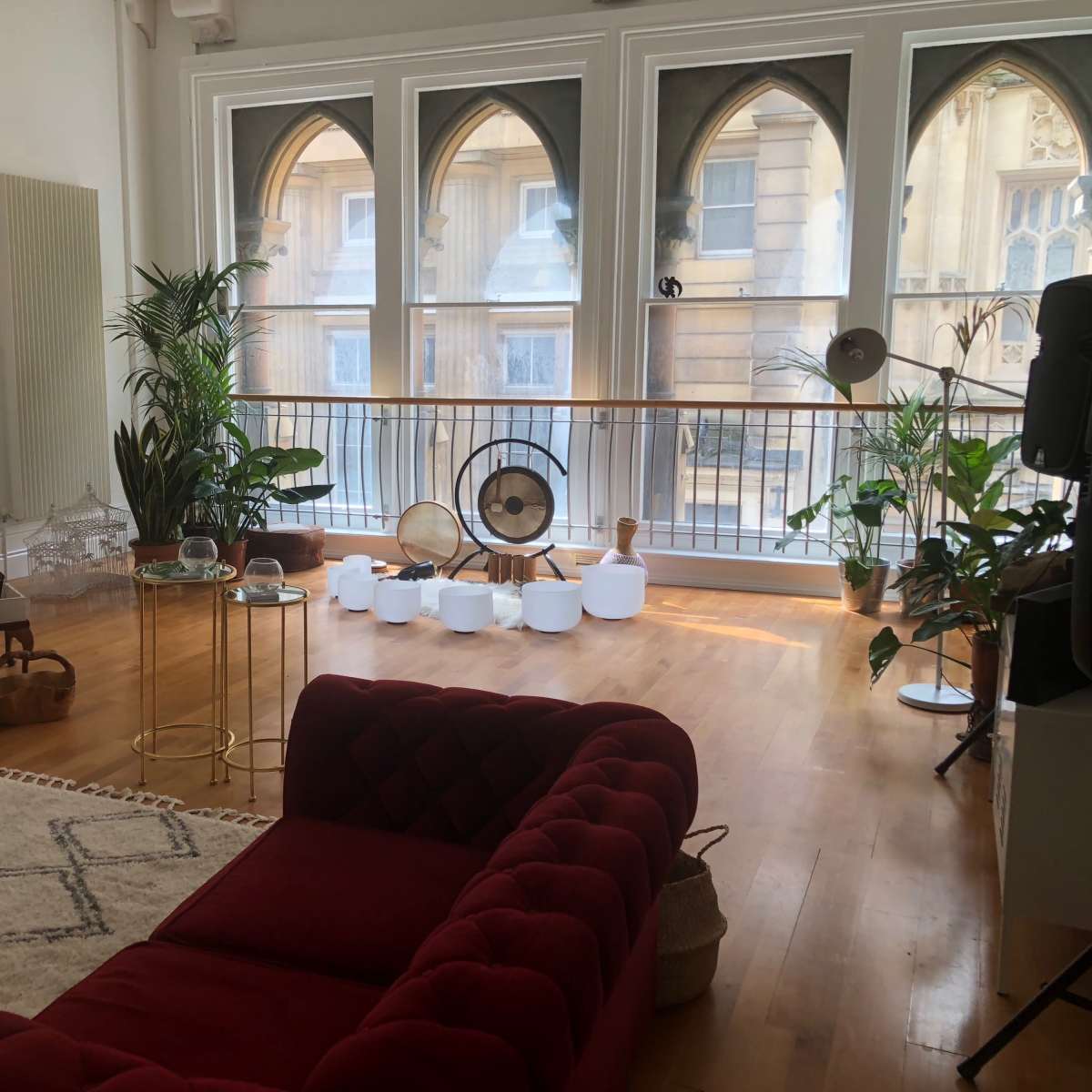 A modern living room with large arched windows, a mix of plants, a red sofa, and various decorative items.