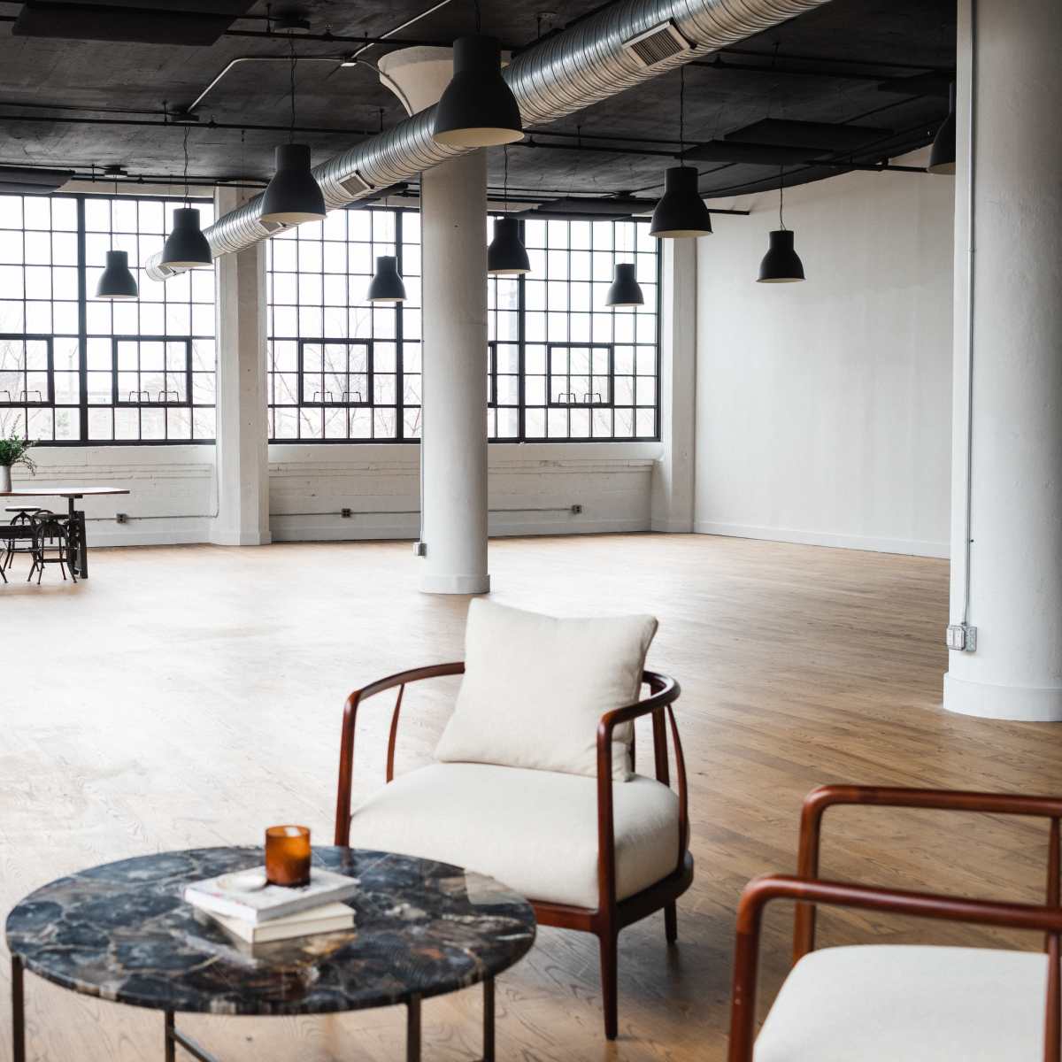 A spacious, modern interior with large windows, minimal furniture, and wooden flooring.