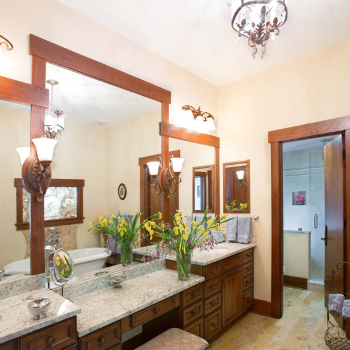 A spacious bathroom featuring dual sinks with a granite countertop, three mirrors, and decorative lighting fixtures.
