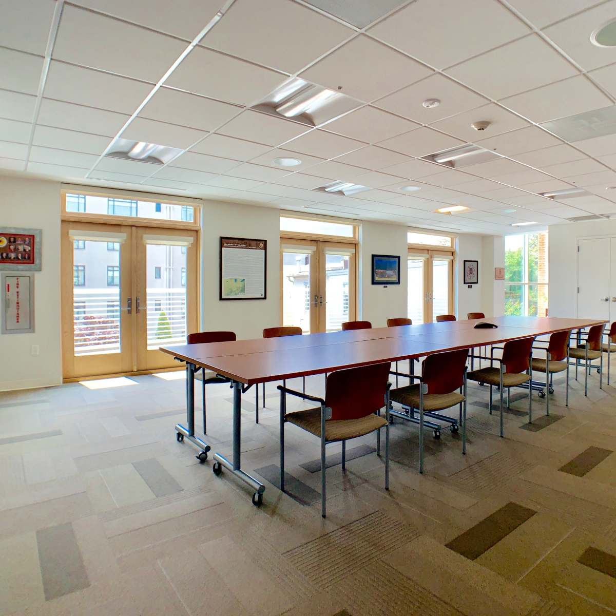 A conference room with a long table surrounded by chairs and large windows letting in natural light.