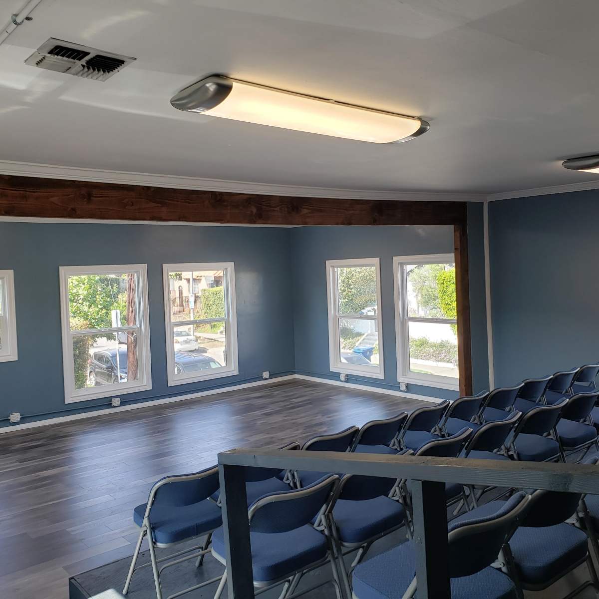 A spacious room with blue walls and a row of blue chairs arranged facing a blank wall, illuminated by overhead lights.