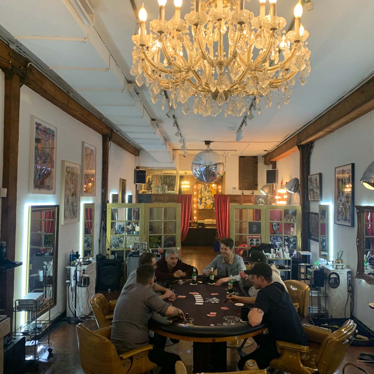 A group of five people are gathered around a round table playing cards in a spacious, well-lit room with modern decor and a chandelier.