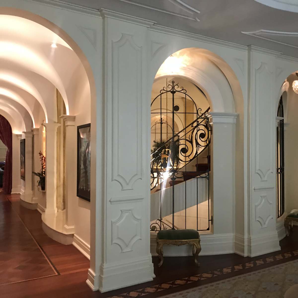 A softly lit hallway with arched doorways and a decorative staircase in the background.
