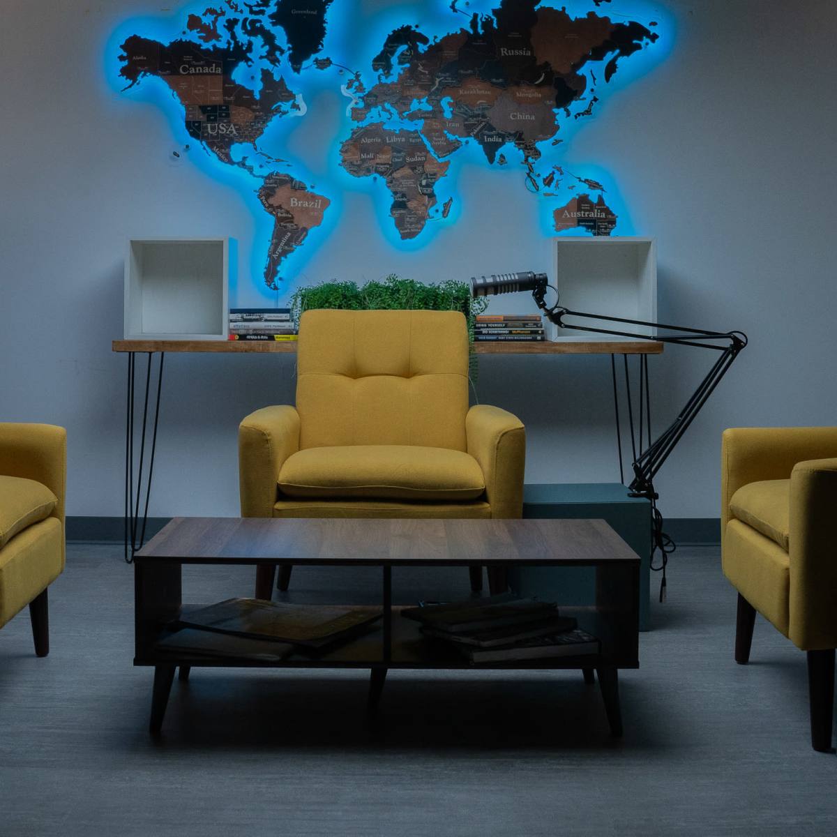A modern podcast studio features three yellow chairs, a wooden coffee table, and a world map illuminated in blue on the wall.