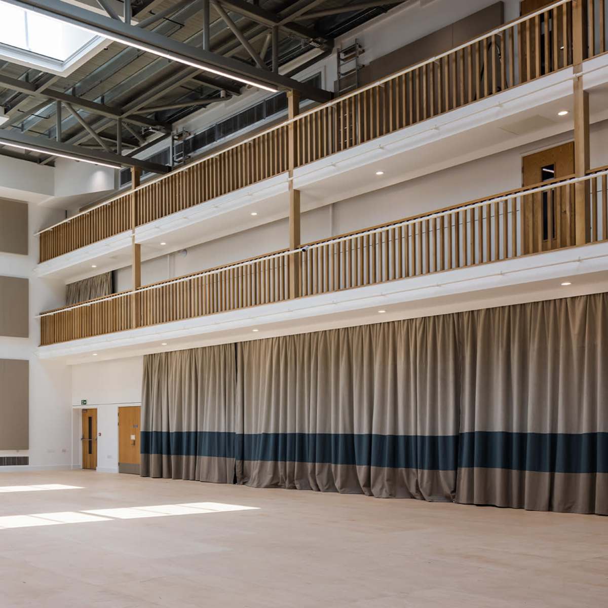 A spacious interior area with high ceilings, large windows, and a stage area draped with curtains.