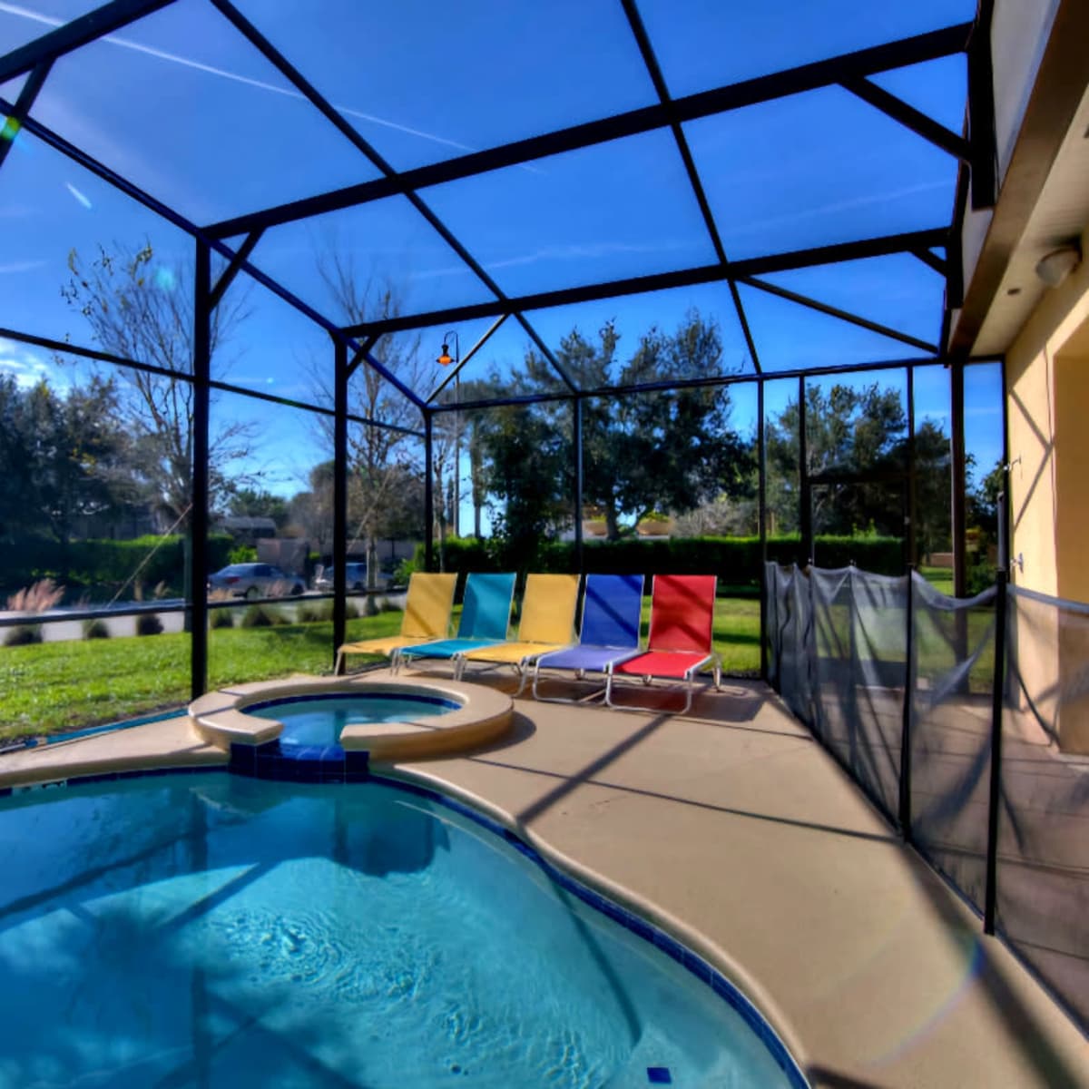 A screened-in pool area featuring a circular hot tub, colorful lounge chairs, and a clear blue sky in the background.