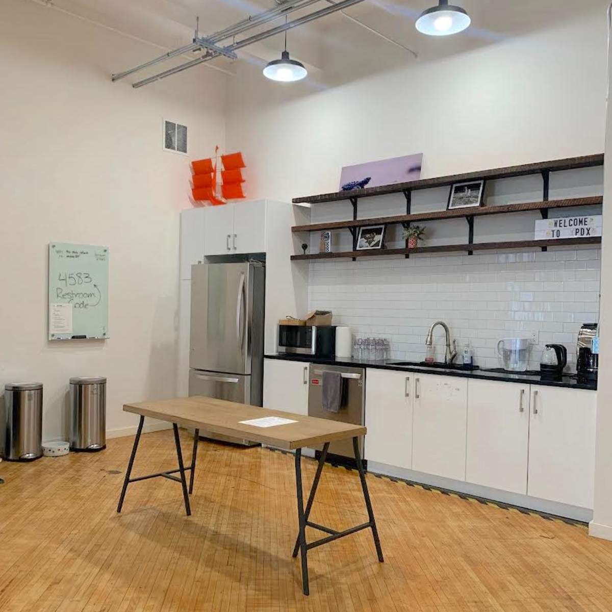 A modern kitchen area with a wooden table, stainless steel appliances, and shelves displaying various items.