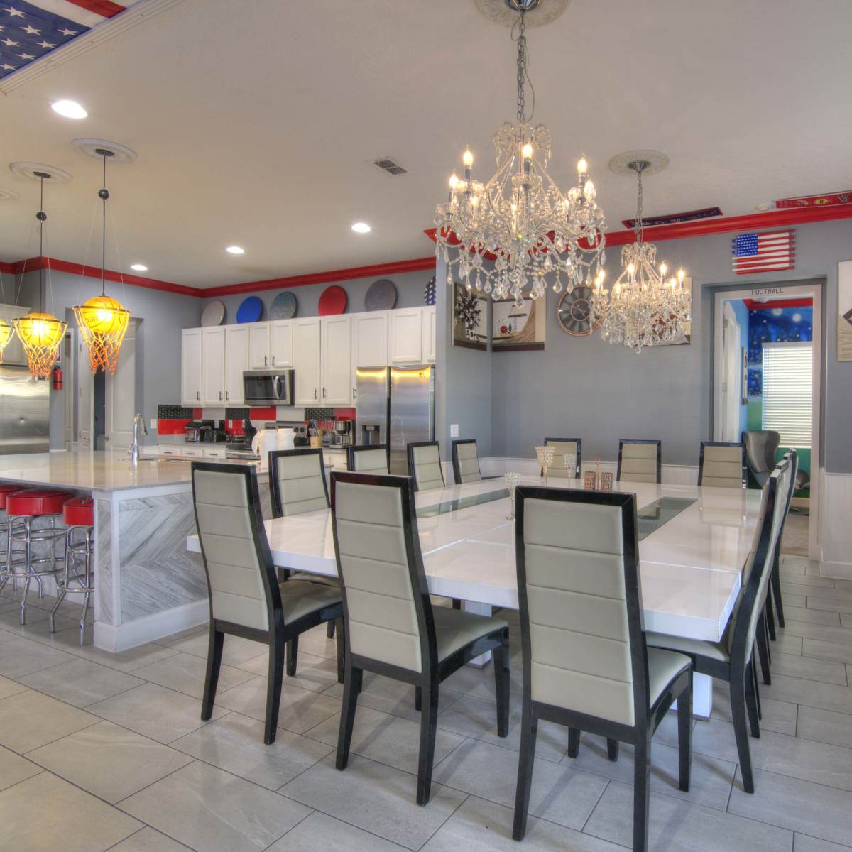 A spacious dining area features a long white table surrounded by black chairs, with modern chandeliers and colorful decorative elements on the ceiling.