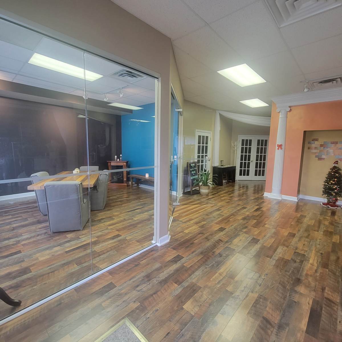 A spacious, divided office area with glass walls, featuring a conference table, chairs, and a decorative Christmas tree in the corner.