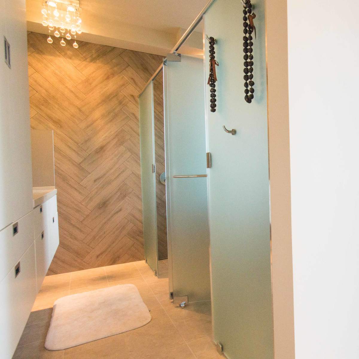 A modern bathroom on the left with a glass shower and herringbone tile, and a blank wall on the right leading to a balcony with a railing.