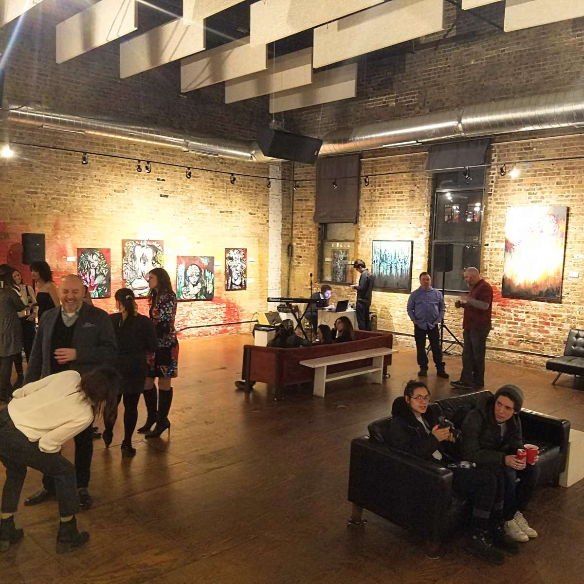 An art gallery event with attendees socializing amidst colorful artwork displayed on the brick walls.