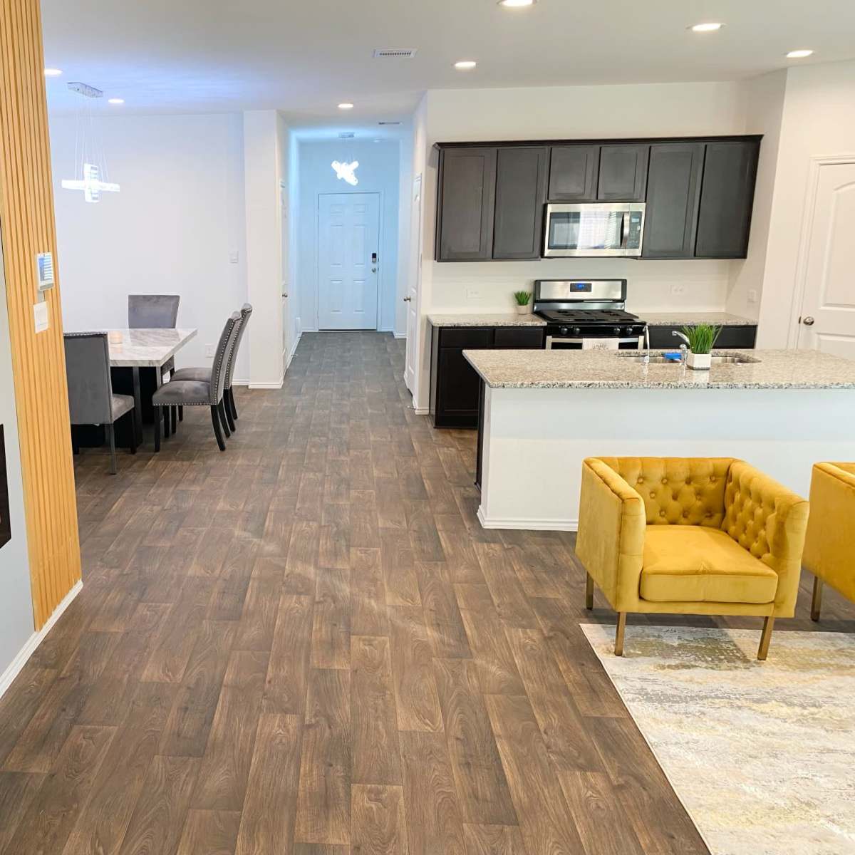 A modern living space featuring a kitchen with dark cabinetry, a dining area with a table and chairs, and a cozy sitting area with a yellow armchair.