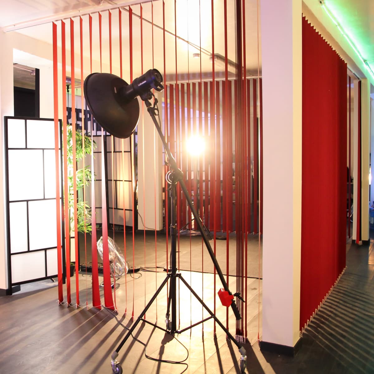 A photography studio with lighting equipment, red and black backdrops, and partitions creating distinct areas.