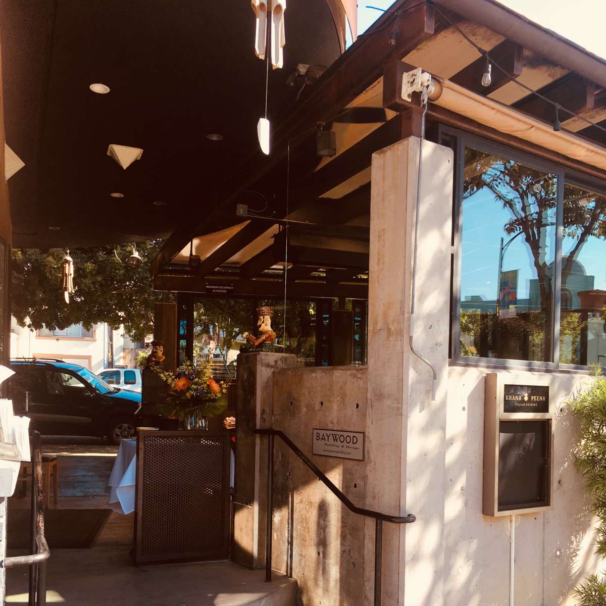 The entrance to a restaurant features a modern concrete and glass design with decorative flowers and a menu display.
