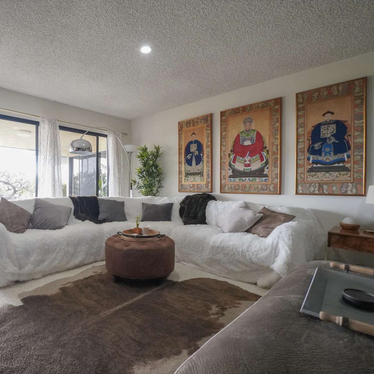 A modern living room features a large white sectional sofa, a round coffee table, and decorative wall art, with sliding glass doors that open to a view of the outdoors.