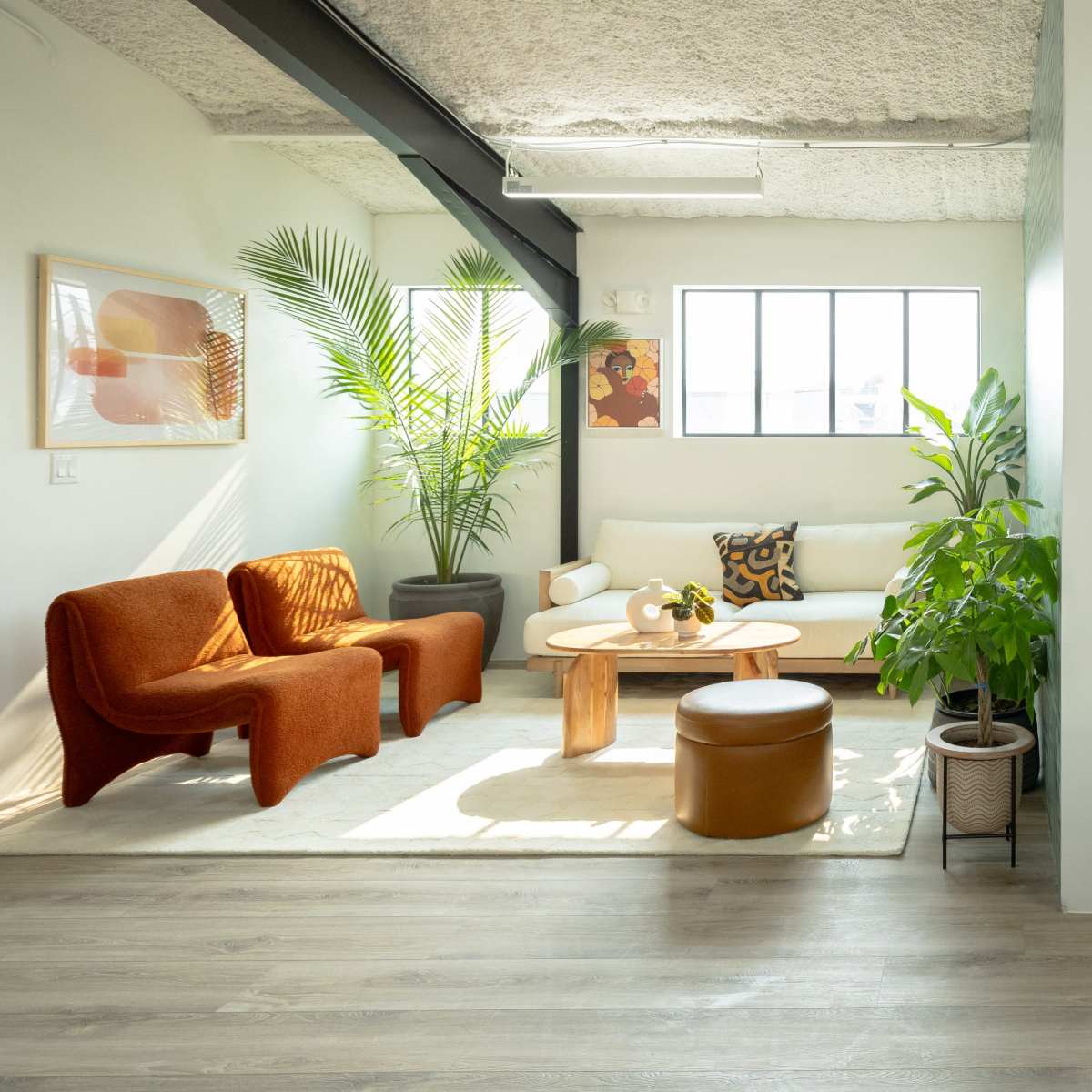 A modern office space divided into a lounge area with orange seating and plants and a meeting area with a circular table and chairs.