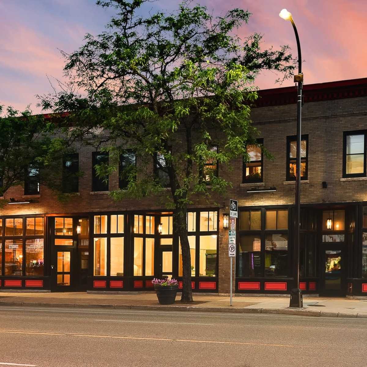 A two-story brick building with large windows, located on a city street at dusk, featuring a red and black color scheme.