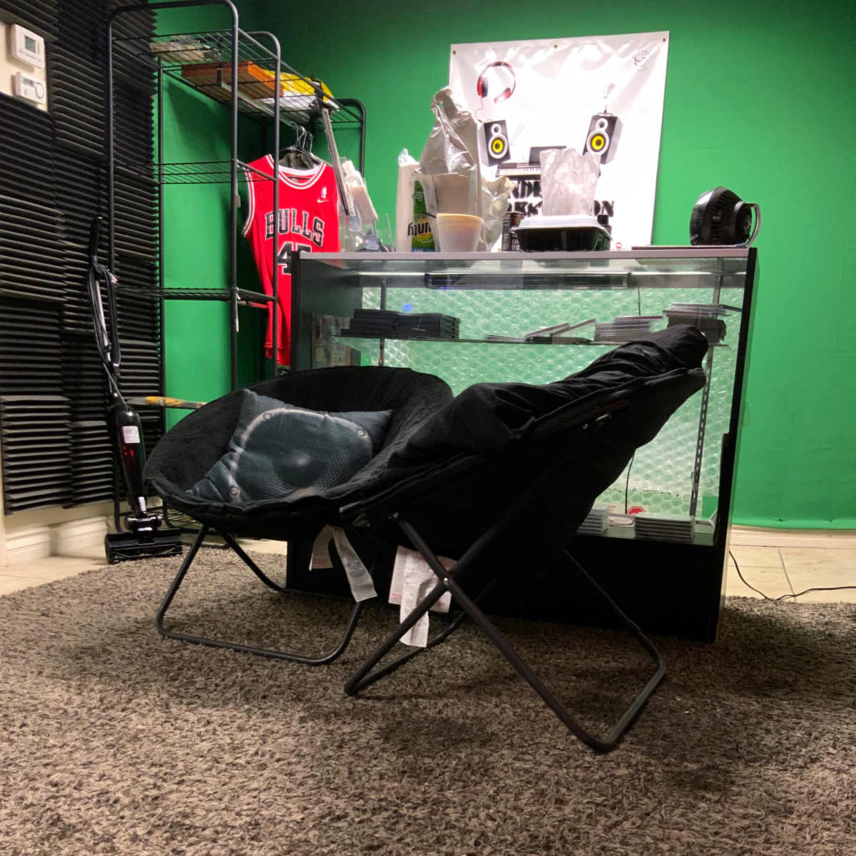 Two folding chairs placed on a carpeted floor in a room with a green backdrop and a display table.