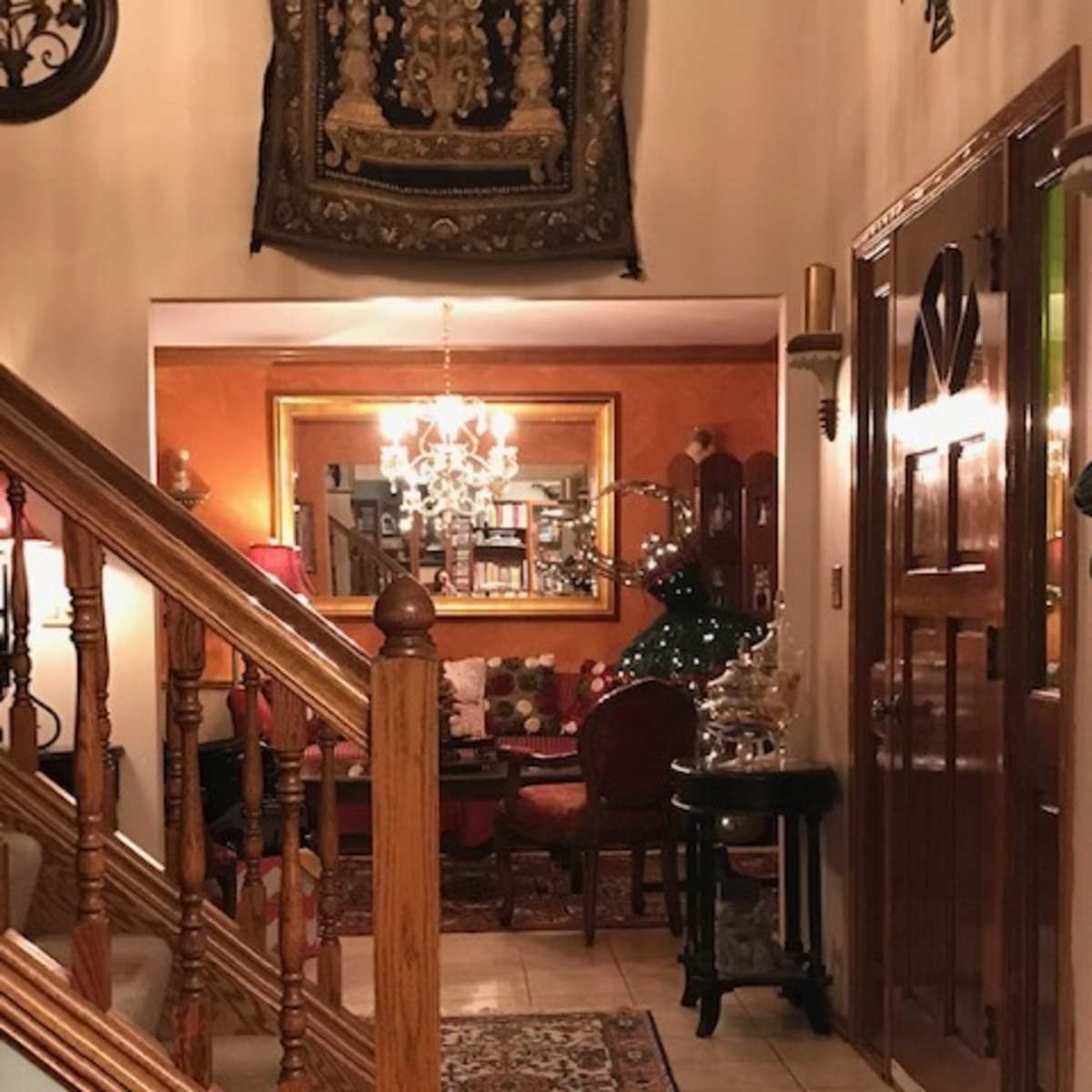 A warmly lit entryway with a wooden staircase, a decorative rug on tiled flooring, and a cozy sitting area visible in the background.