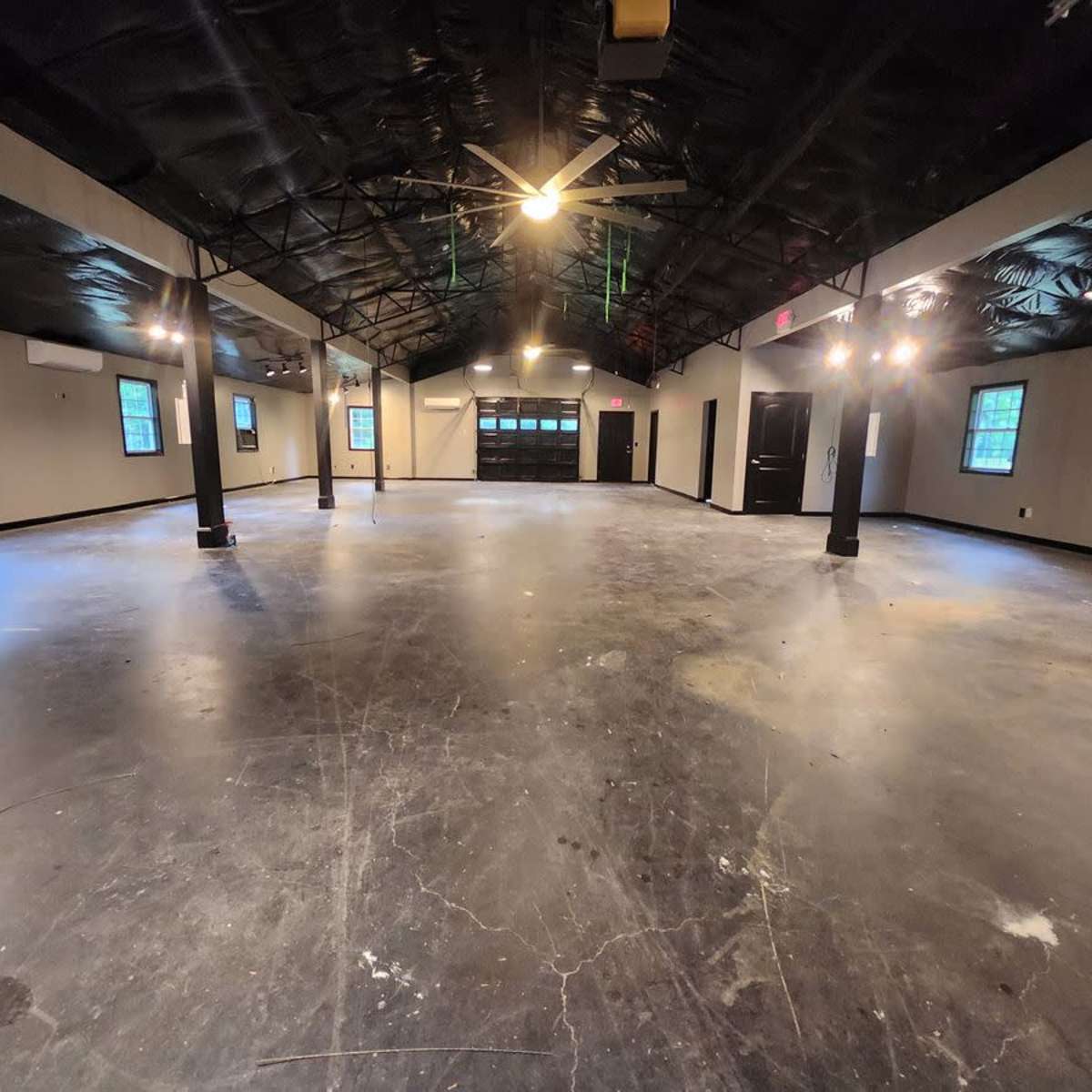A spacious, empty interior area with a polished concrete floor, black beams, and multiple windows.