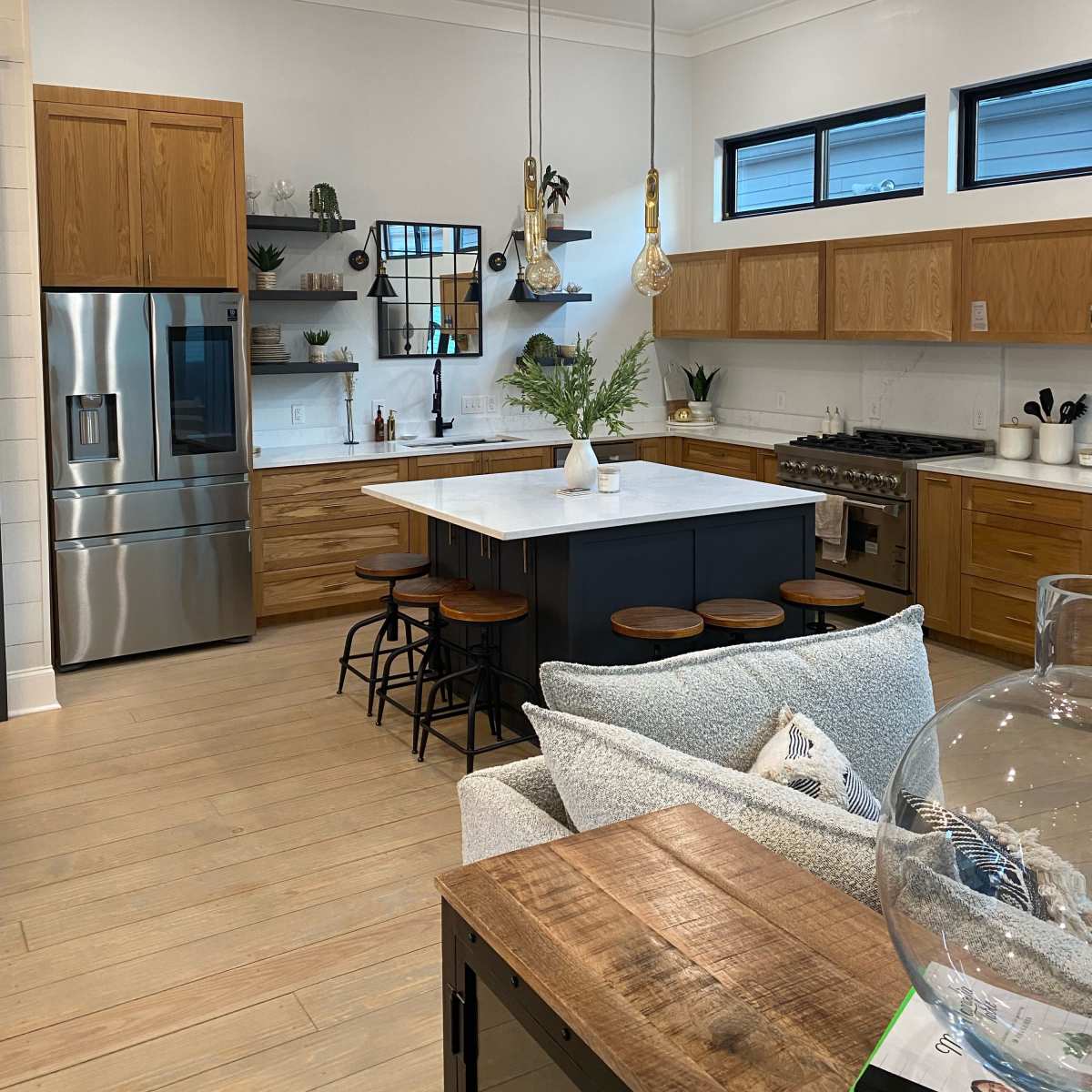 A modern kitchen with wooden cabinets, a large island with seating, and pendant lights overhead.