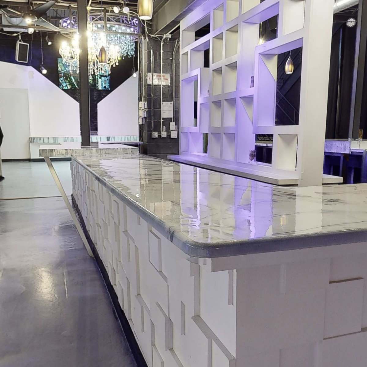 A modern bar area with a marble countertop and a staircase in the background, set in an illuminated venue.