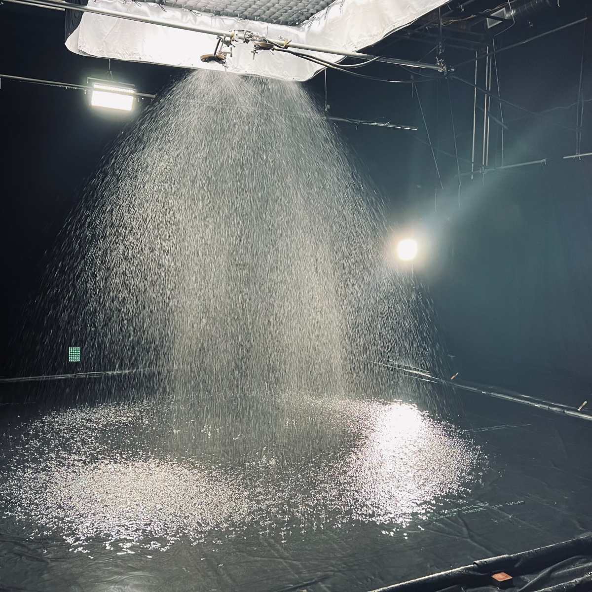 A water spray system creates a circular pool of water on a black surface in a dimly lit studio.