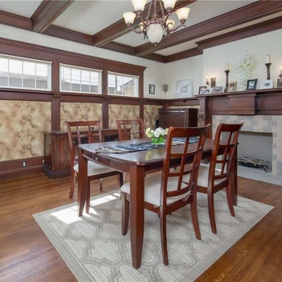 A dining room features a wooden table surrounded by chairs, with a fireplace and paneled walls adorned with decorative accents.