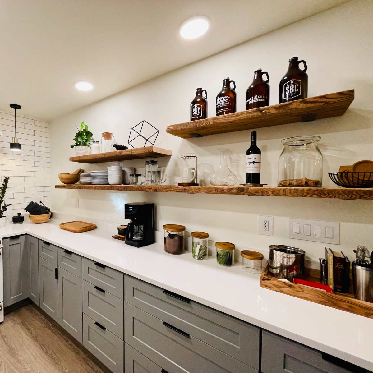 A modern kitchen features a white stove, open wooden shelves with various kitchen items, and a clean countertop with a coffee maker and decorative plants.