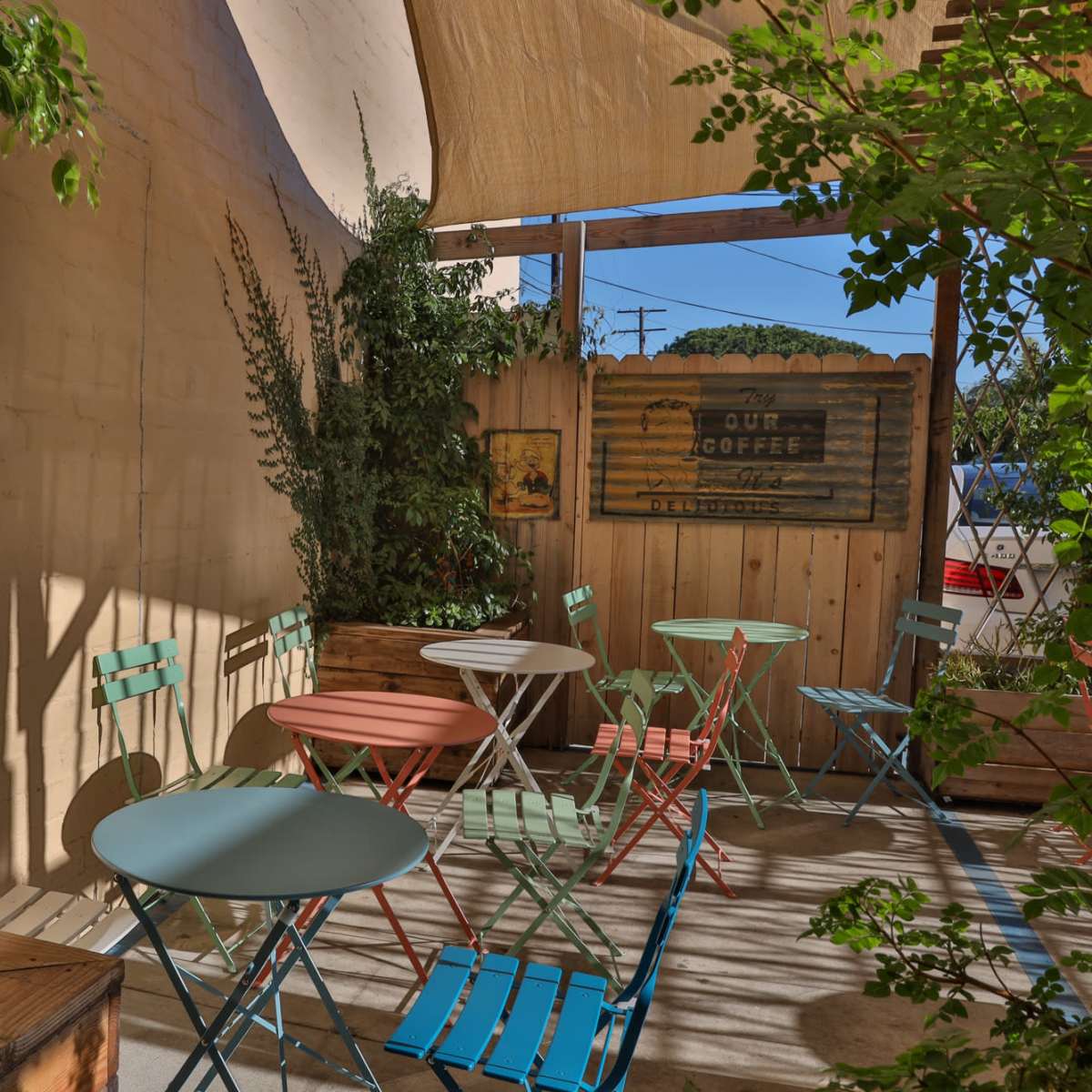 A small outdoor café area with colorful metal chairs and tables surrounded by greenery and wooden fencing.