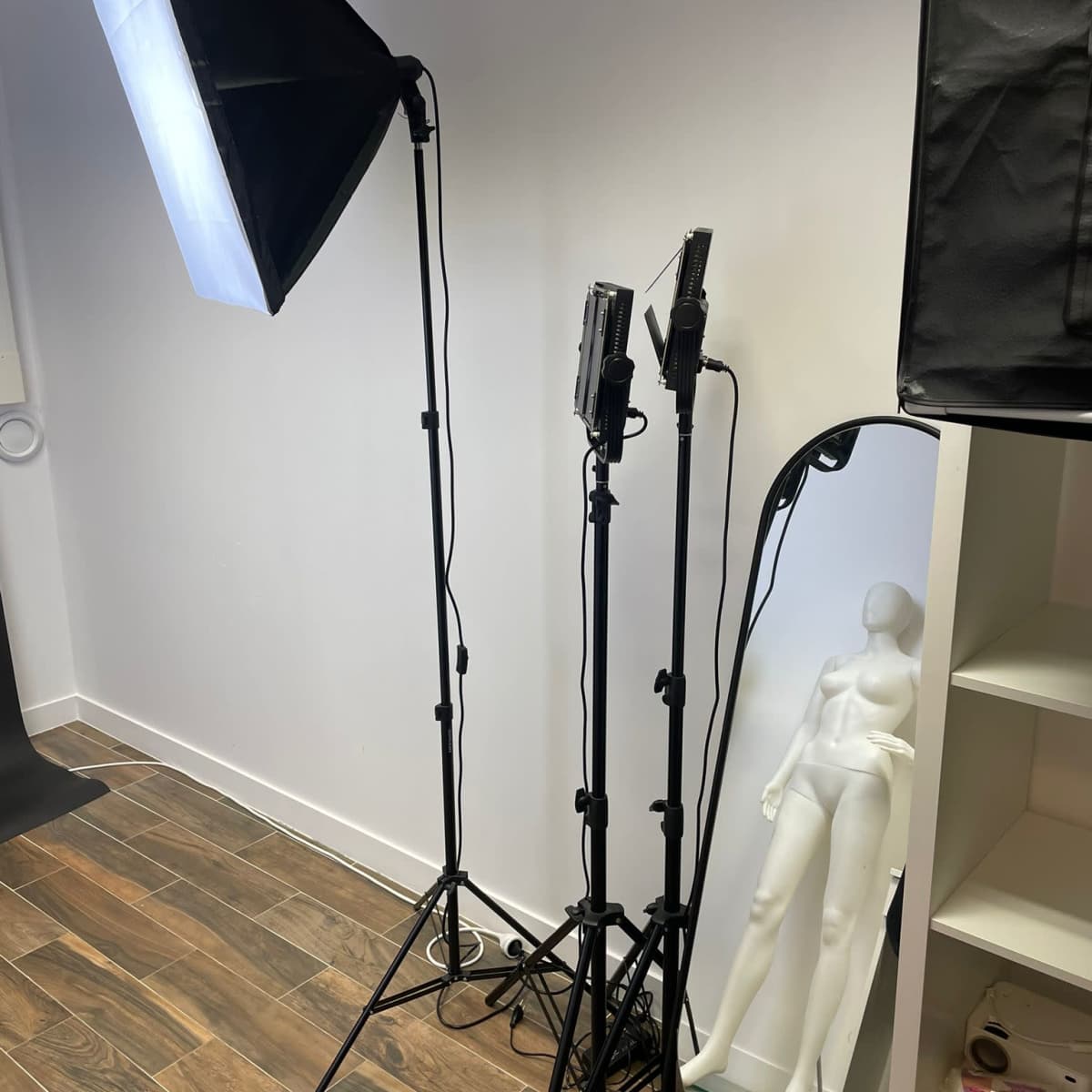 A photography setup with two softbox lights and a mannequin next to a full-length mirror against a white wall.