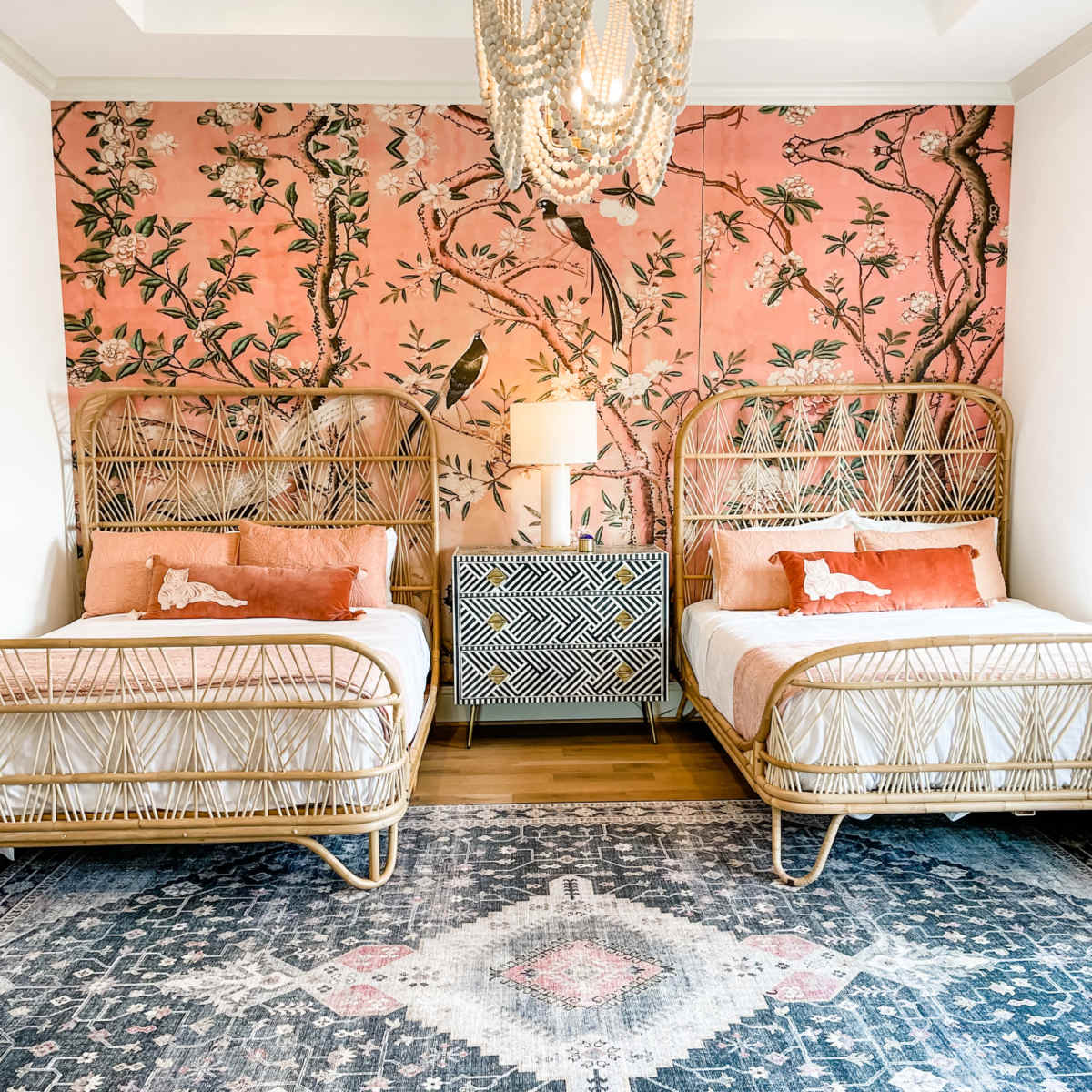 A bedroom with two wicker beds, a patterned area rug, and a floral wallpaper backdrop.