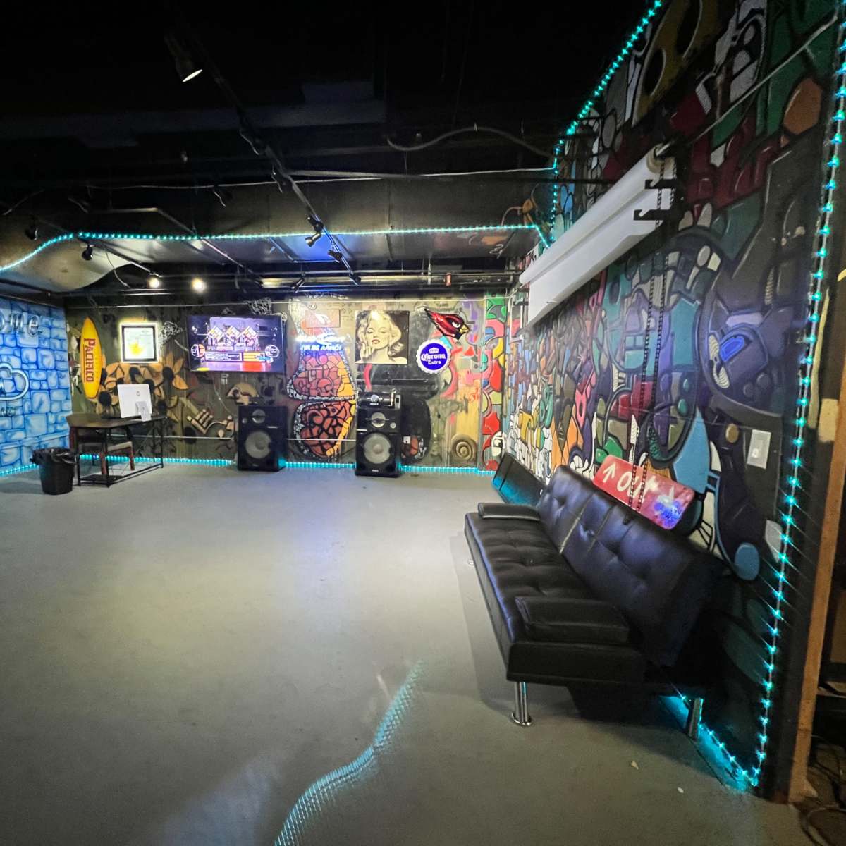 An urban-themed room with colorful graffiti murals, a black couch, and audio equipment placed against the walls.