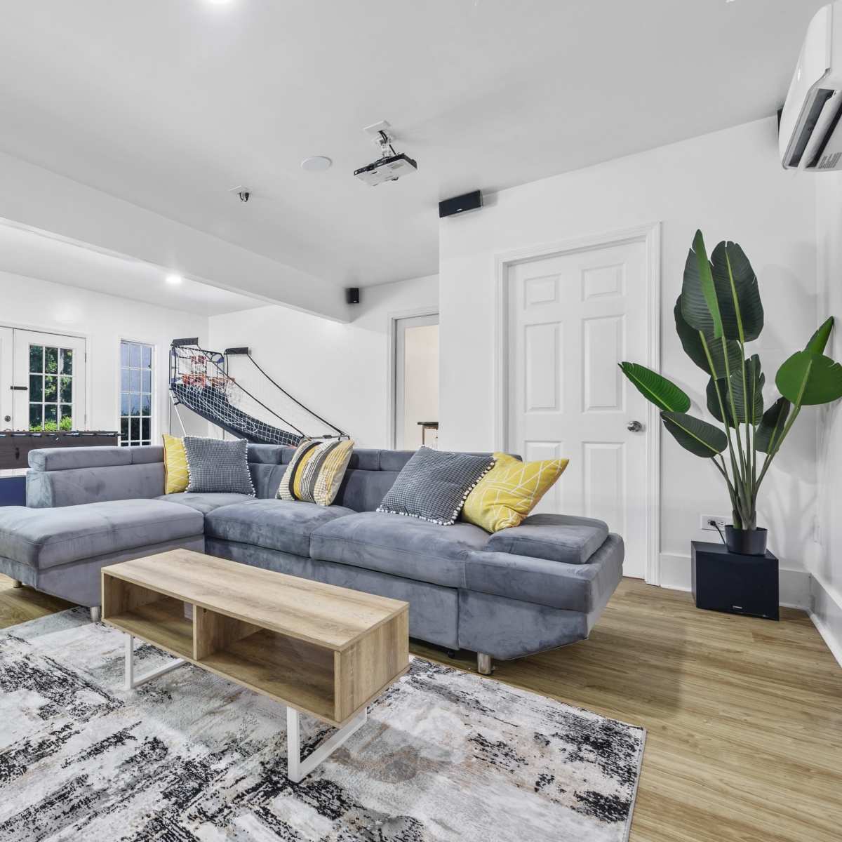 A modern living room with a gray sectional sofa, a wooden coffee table, and large windows that provide ample natural light.