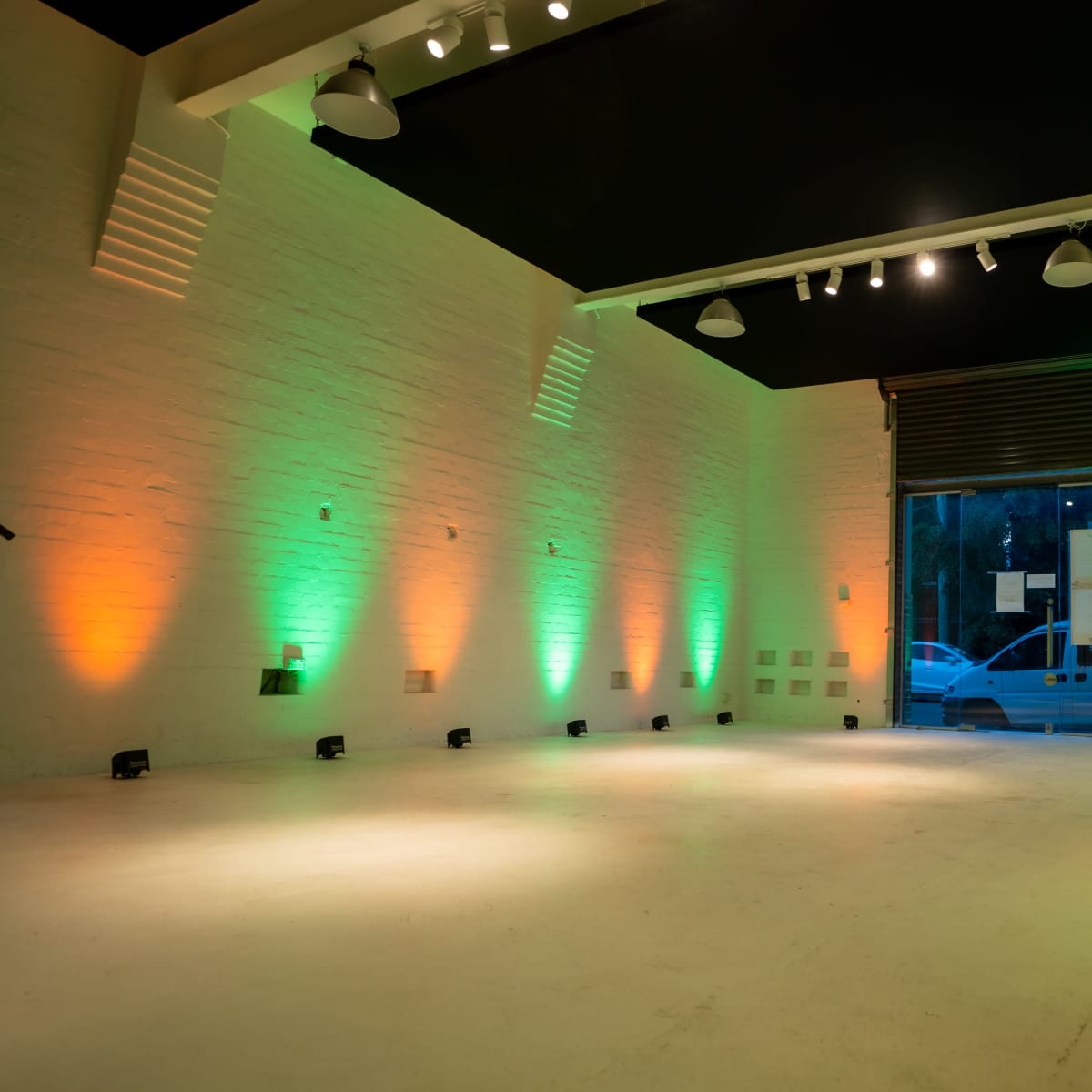 The interior of a spacious, well-lit room features green and orange lighting along the walls, with an open entrance visible at the far end.