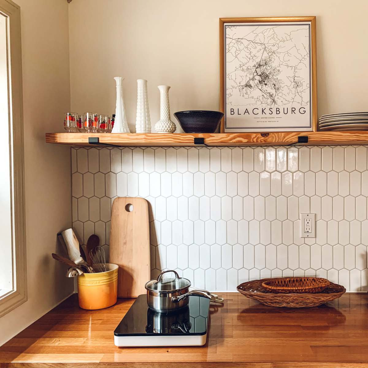 A kitchen countertop with a stove, cooking pot, wooden cutting board, decorative shelves, and potted plants.