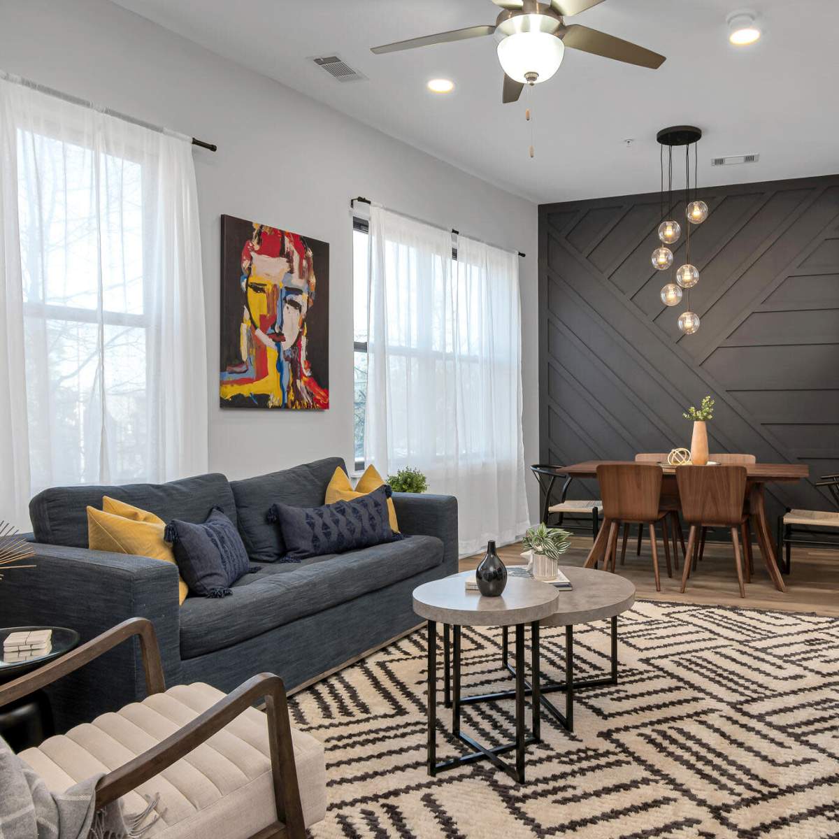 A modern living room with a blue sofa, a round coffee table, and a dining area featuring a wooden table and chairs, all set against a backdrop of large windows and stylish wall designs.