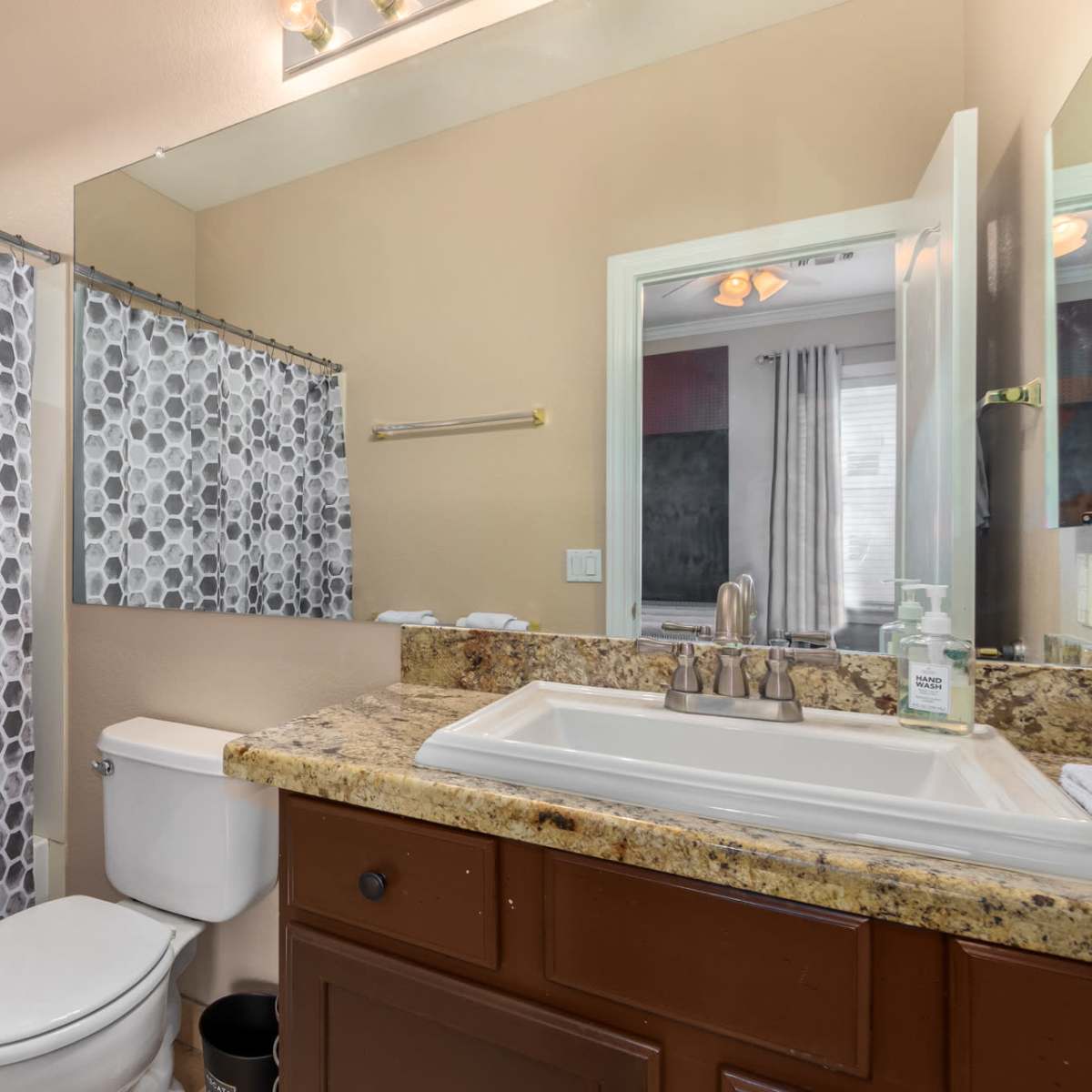 A bathroom featuring a granite countertop, a white sink, a toilet, and a shower curtain with a hexagonal pattern.