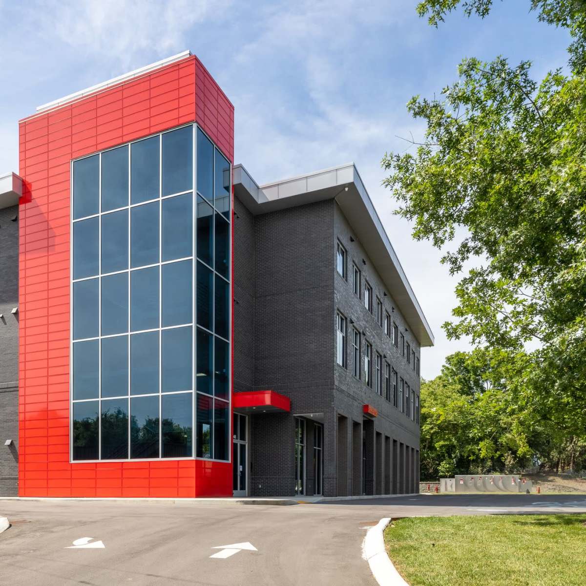 A modern, multi-story commercial building features a combination of dark brick and a large red panel with extensive glass windows.